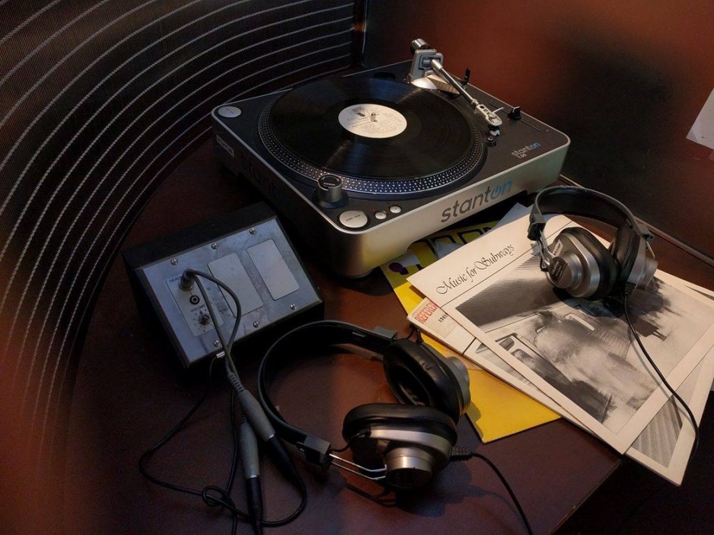 Table with record player, two sets of headphones and various record covers.