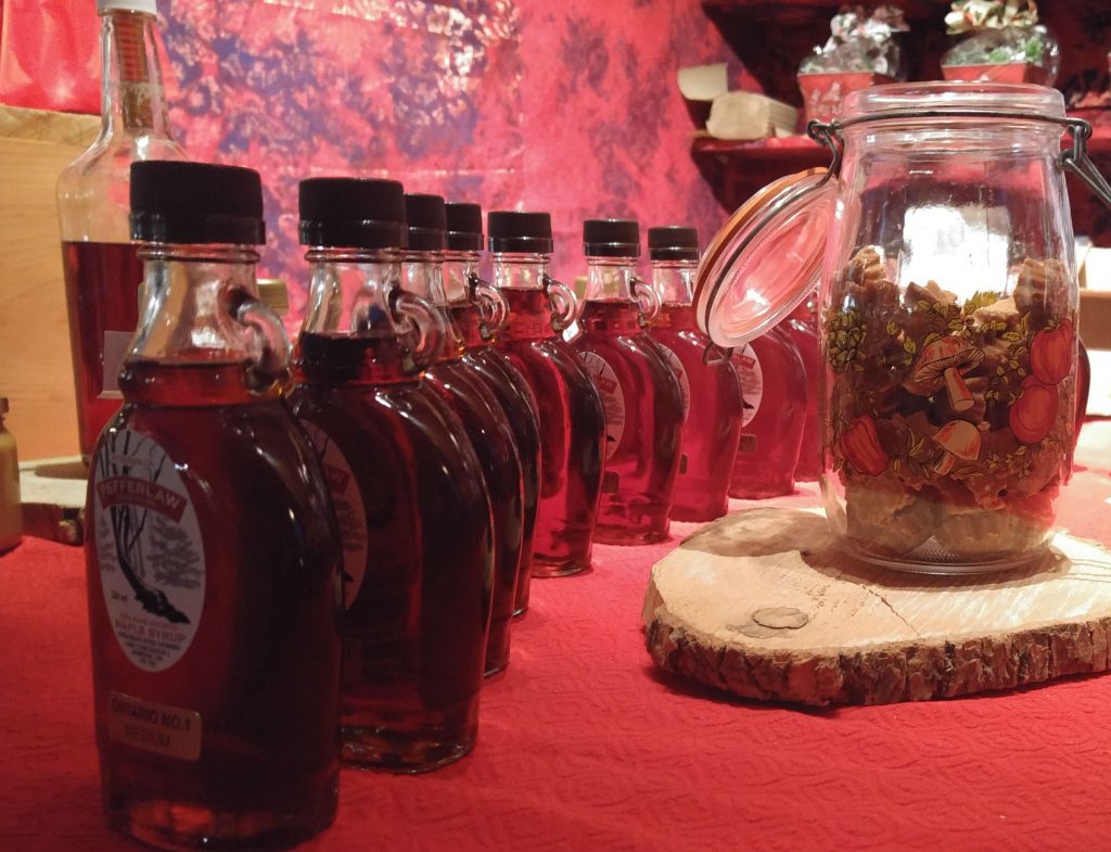 Bottles of maple syrup next to jar on red tablecloth.