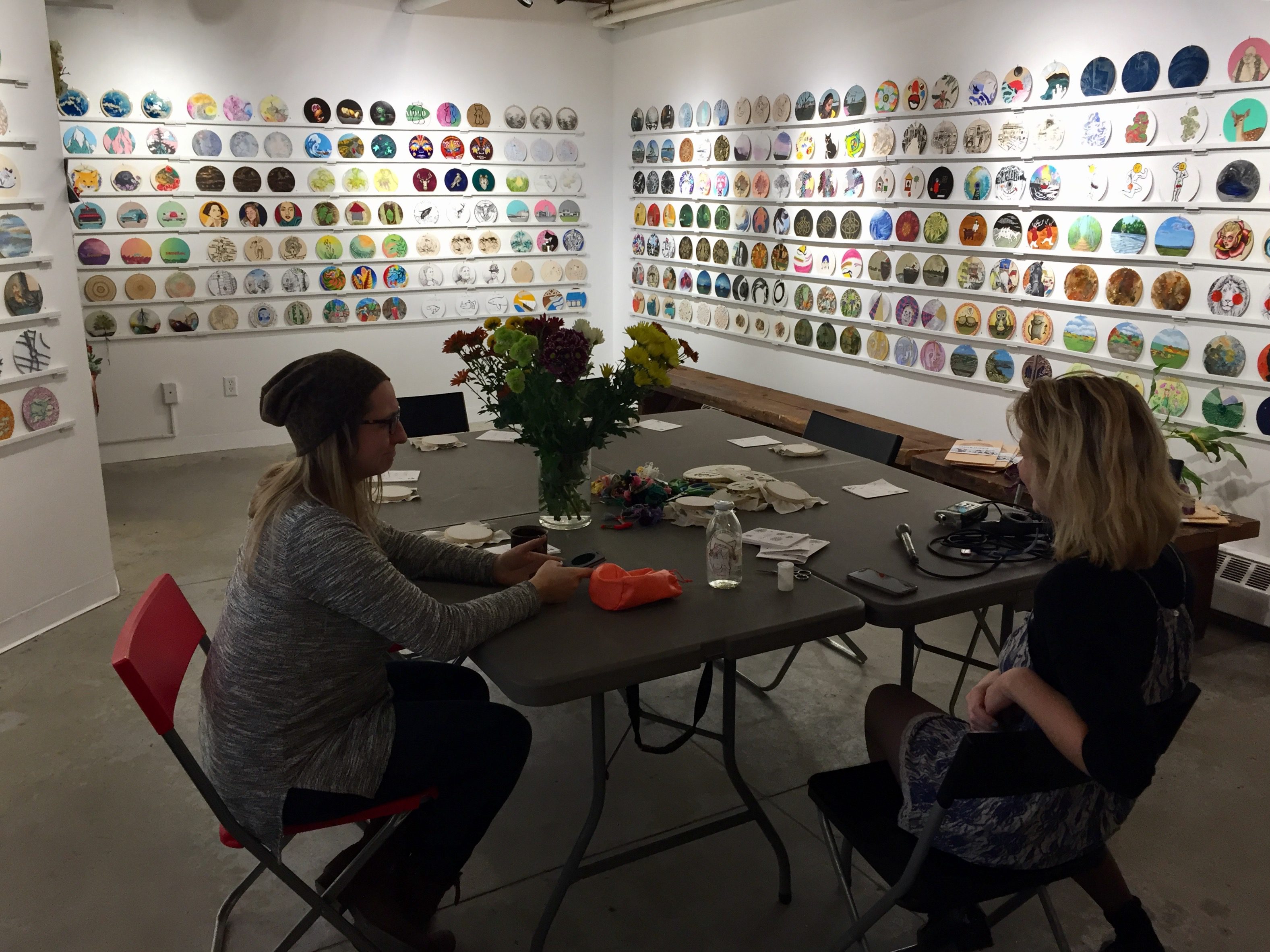 Two women in workshop stitching surrounded by art