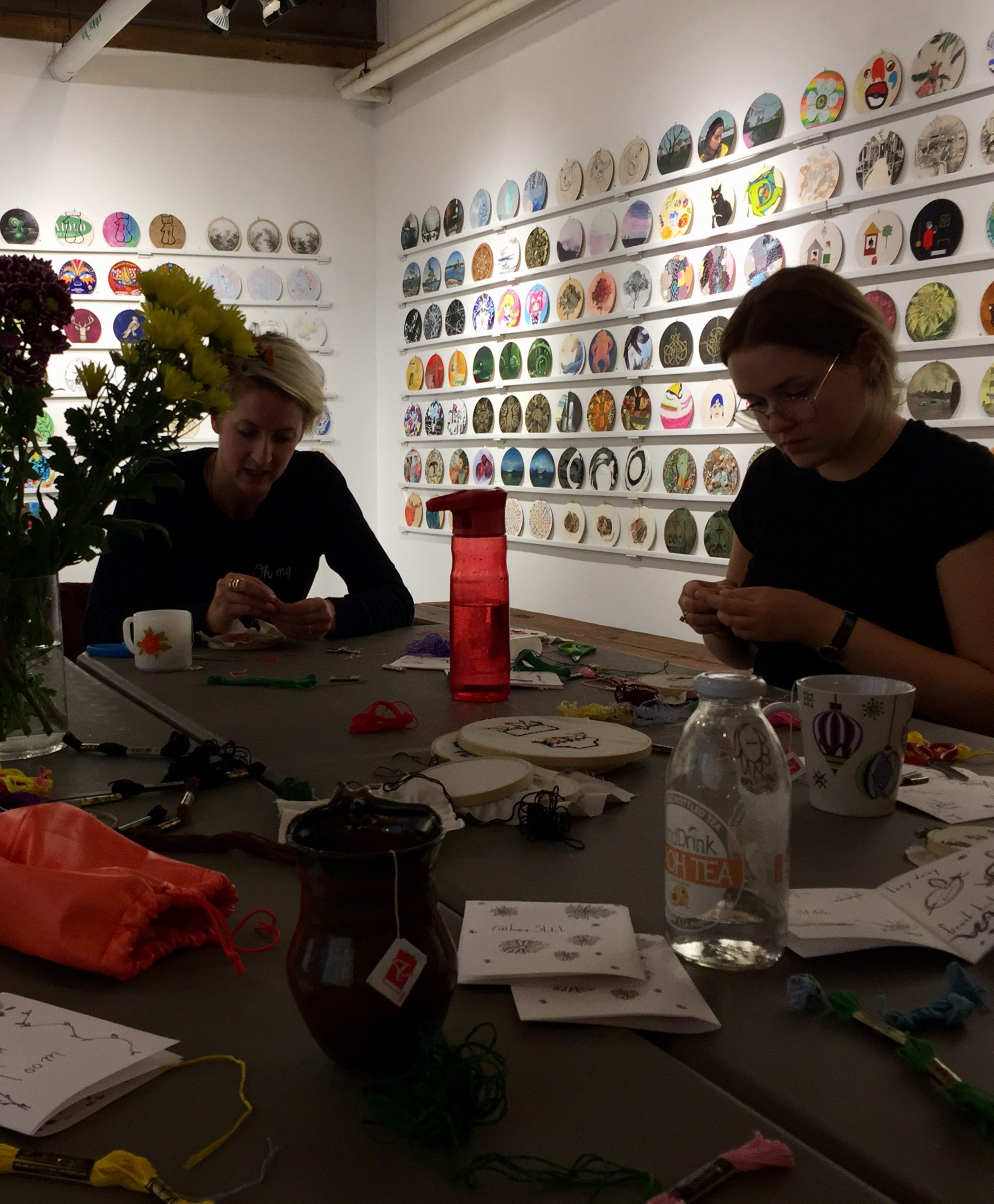 Two women in workshop stitching surrounded by art