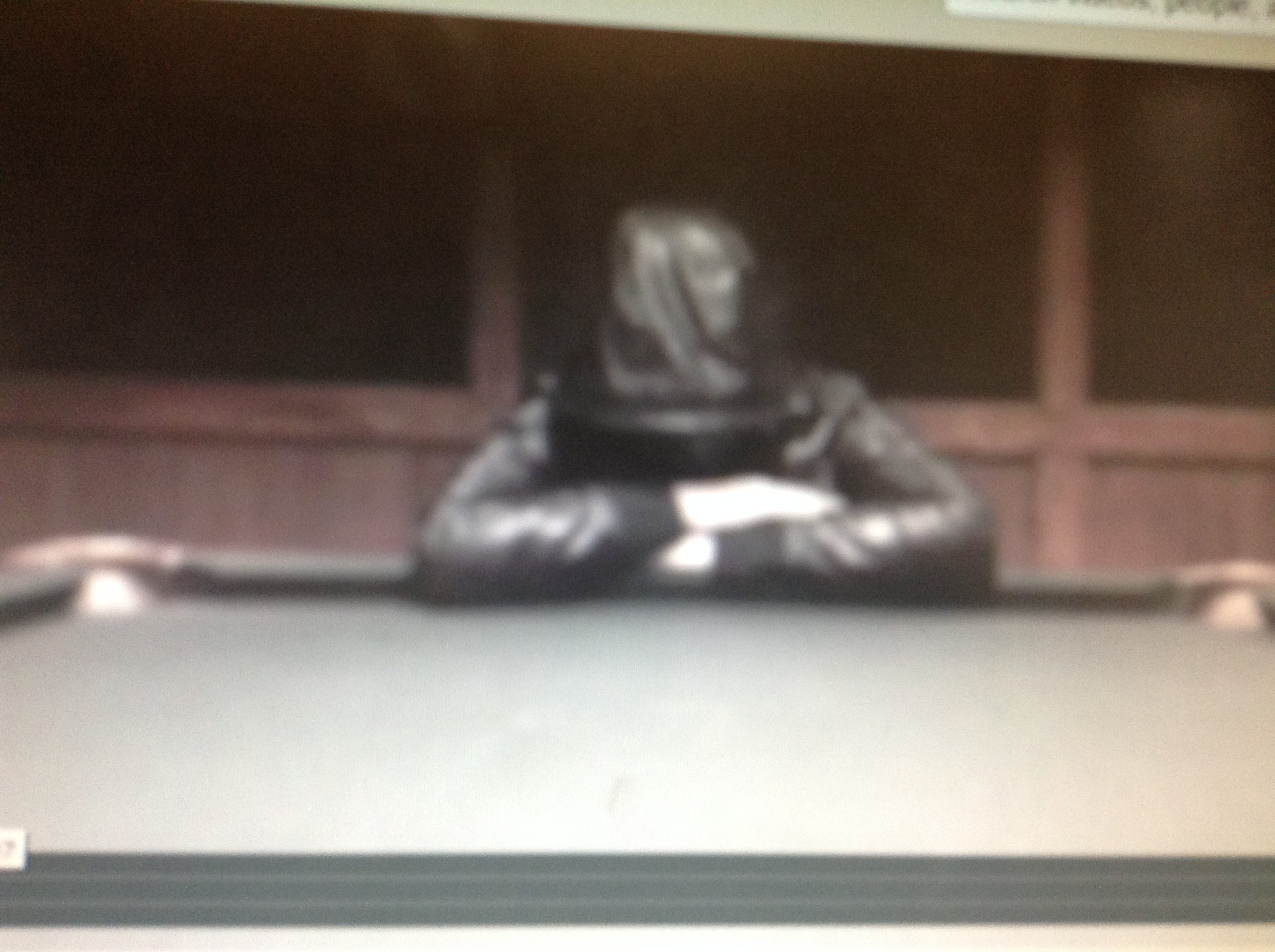 Blurred image of person in black jacket leaning cross armed and hooded leaning on pool table.