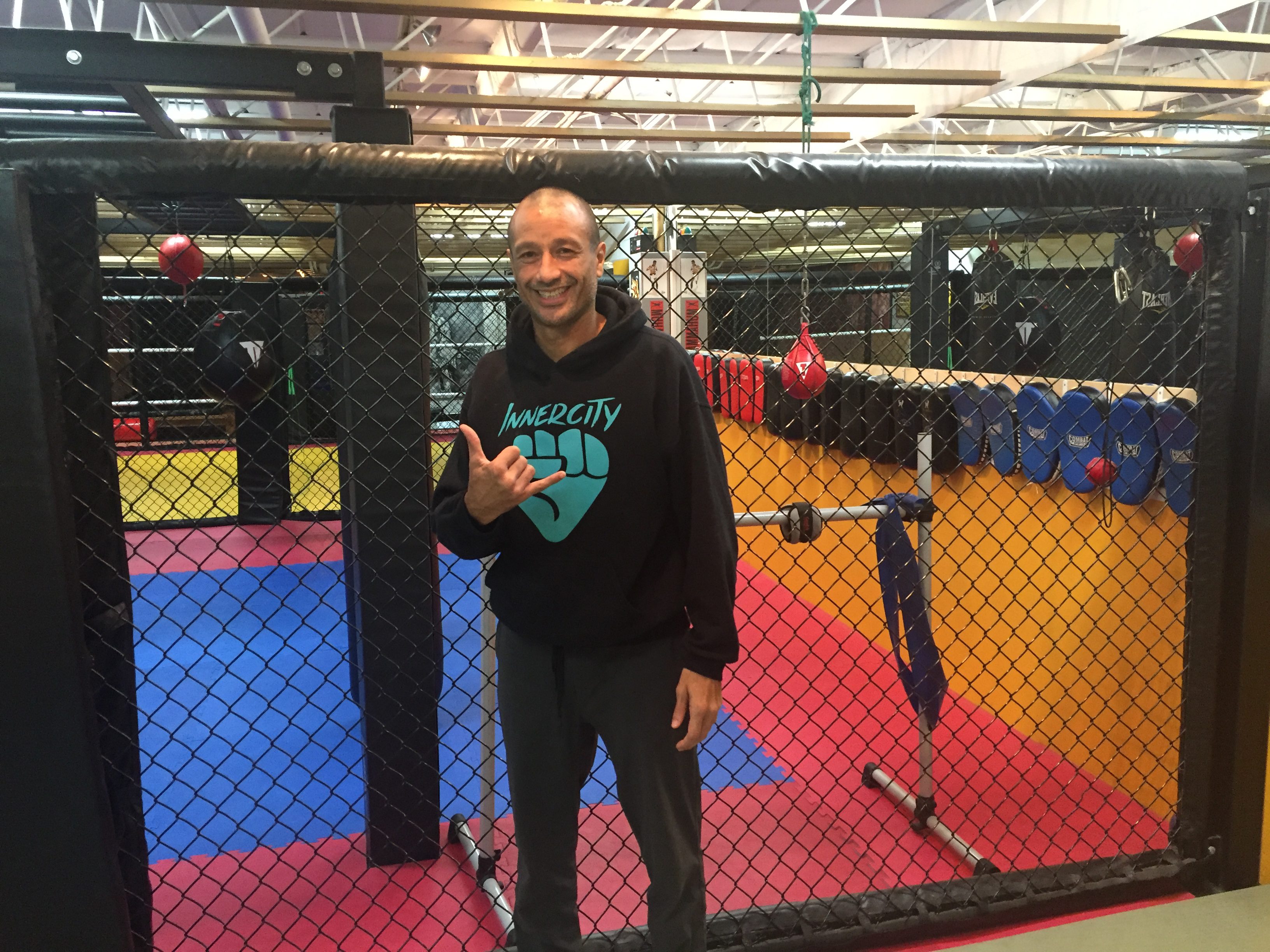 InnerCity MMA instructor Shah Franco standing in gym doing "hang loose" sign.