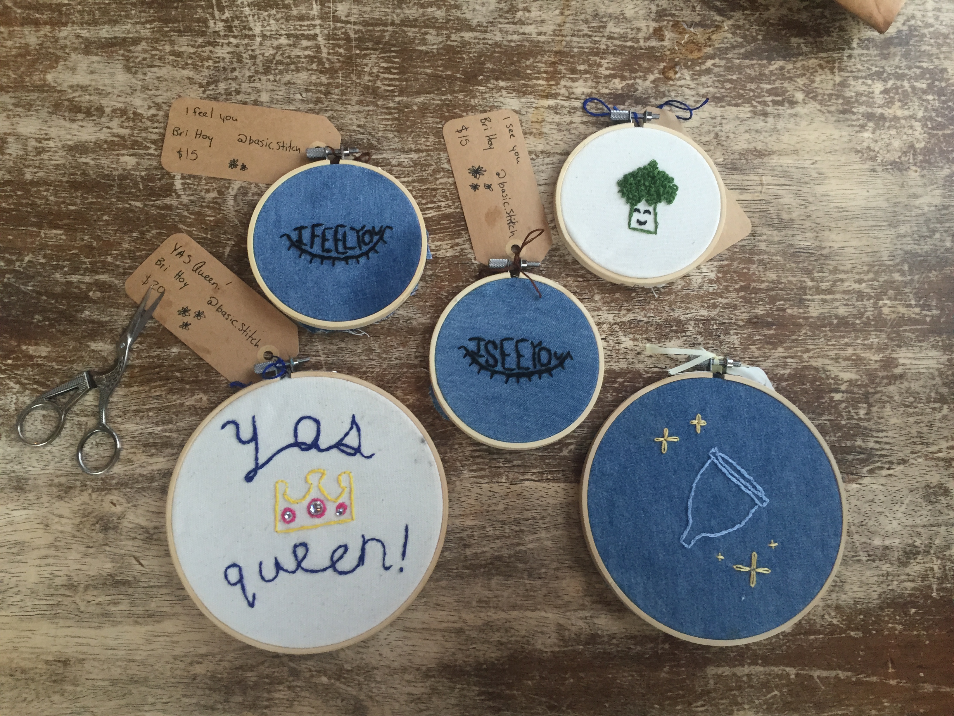 Five cross-stitch pieces on a wood table.