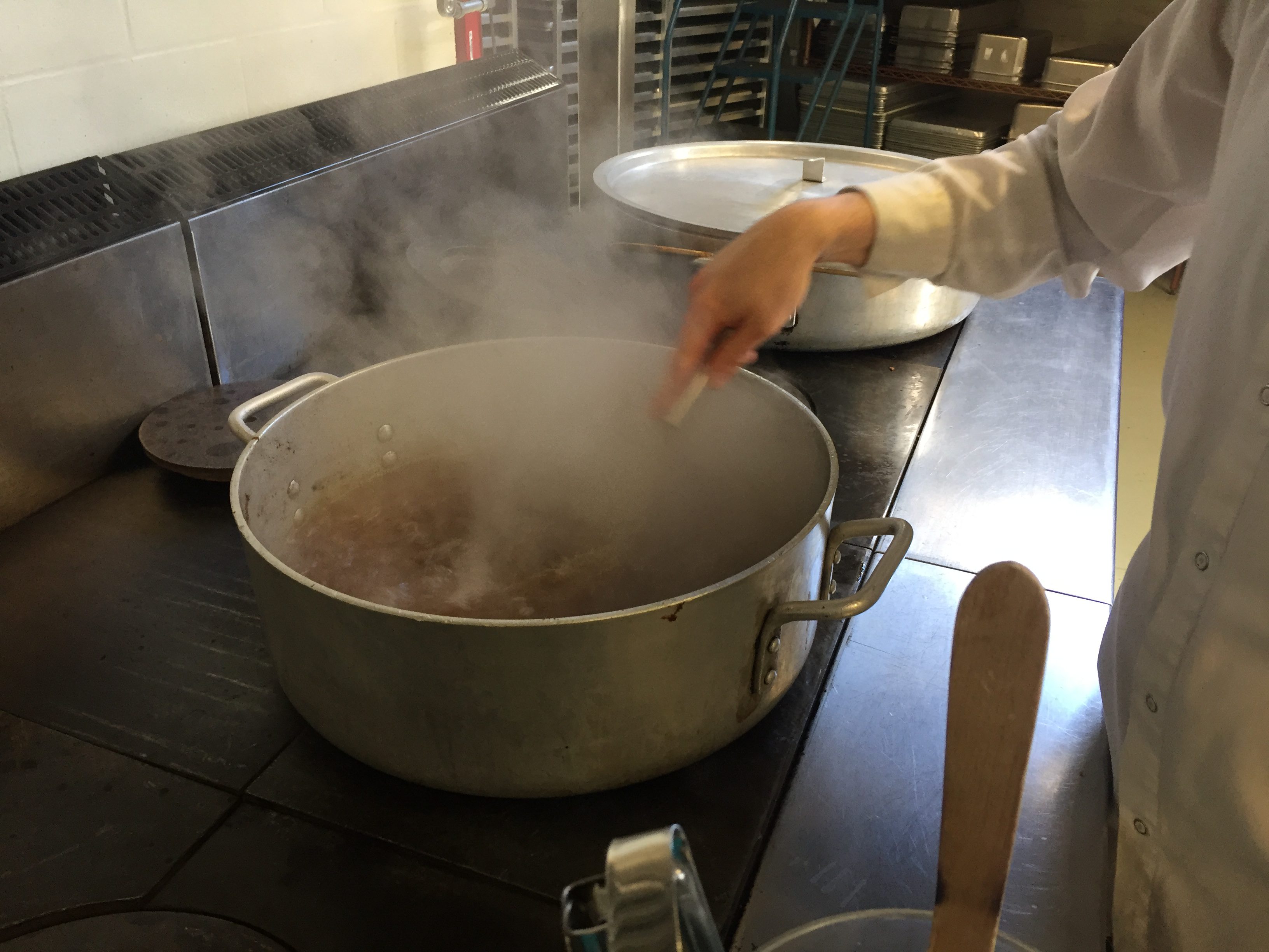 Volunteer cook stirring large pot of broth with whisk.