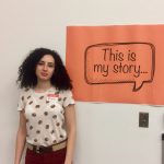Einav Simoni against wall with orange poster that says "This is my story" in speech bubble.