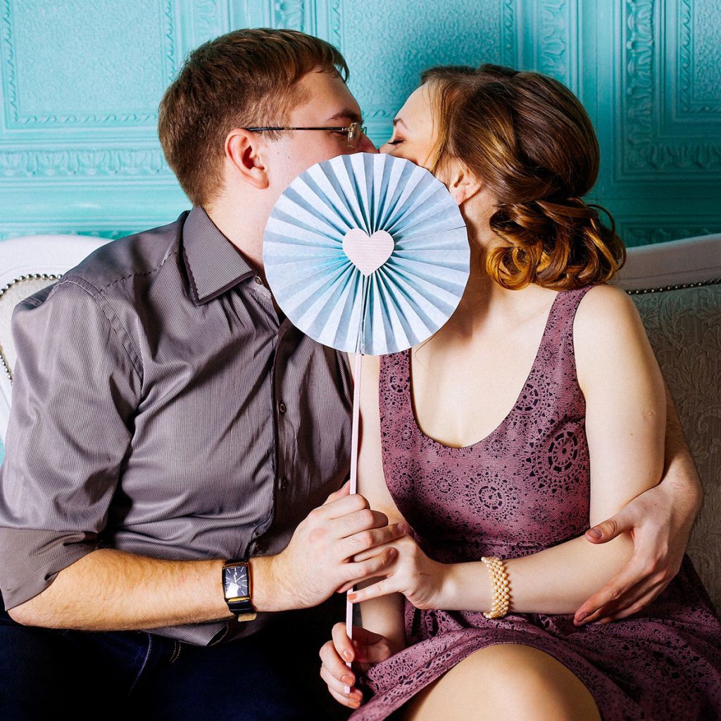 Man and woman kissing behind fan with heart in middle.