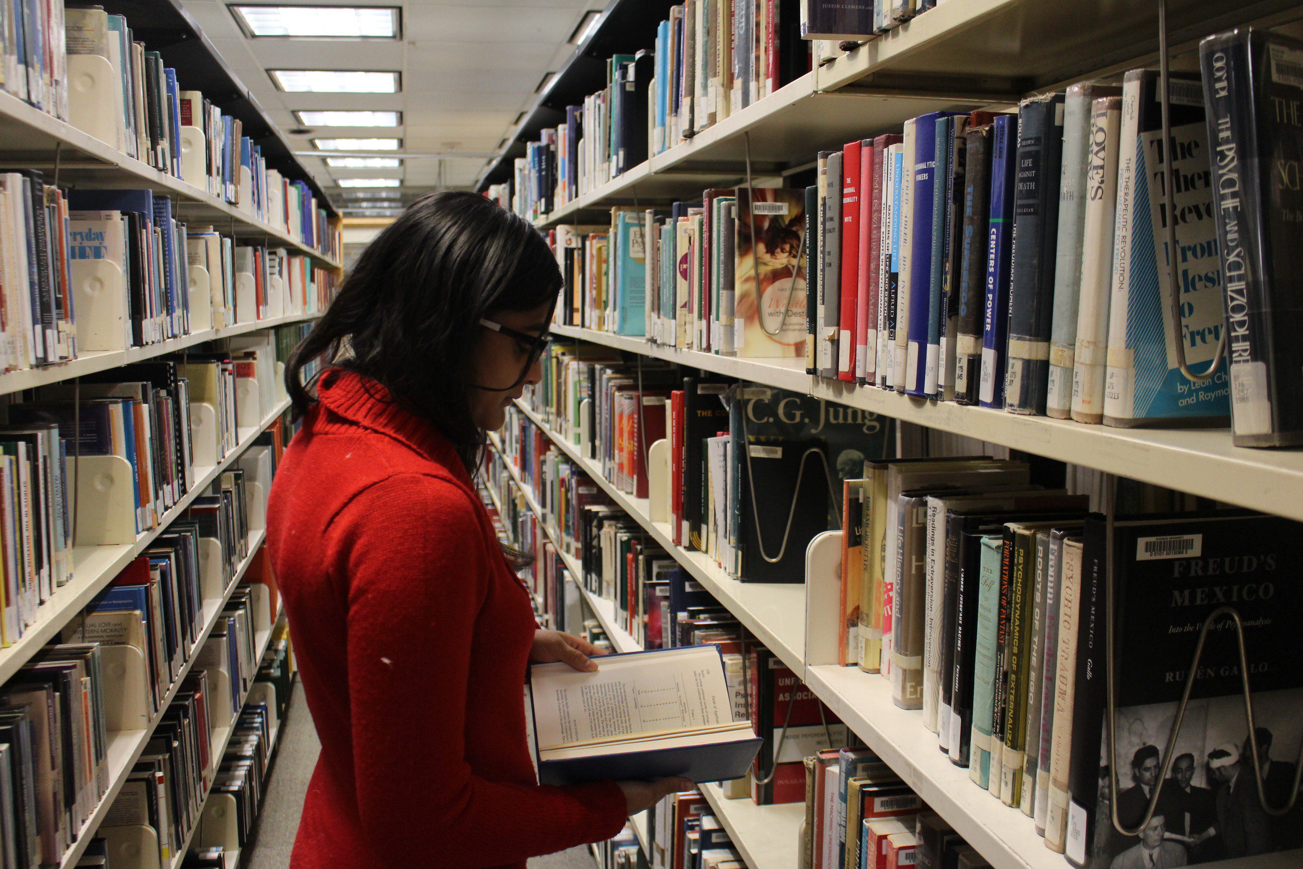 Woman in library aisle looking at book.