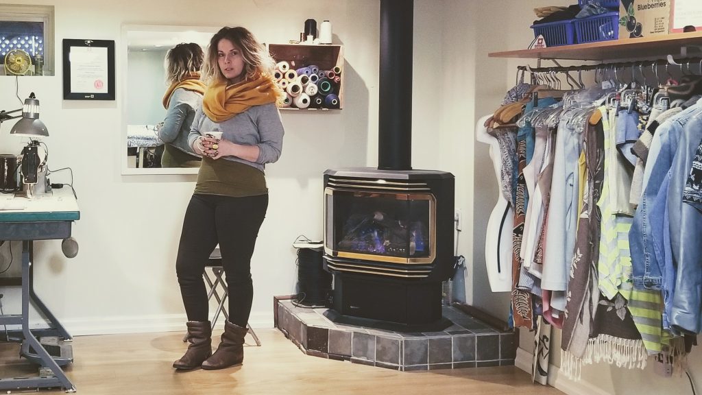 Woman standing next to fire place and large rack of clothing.