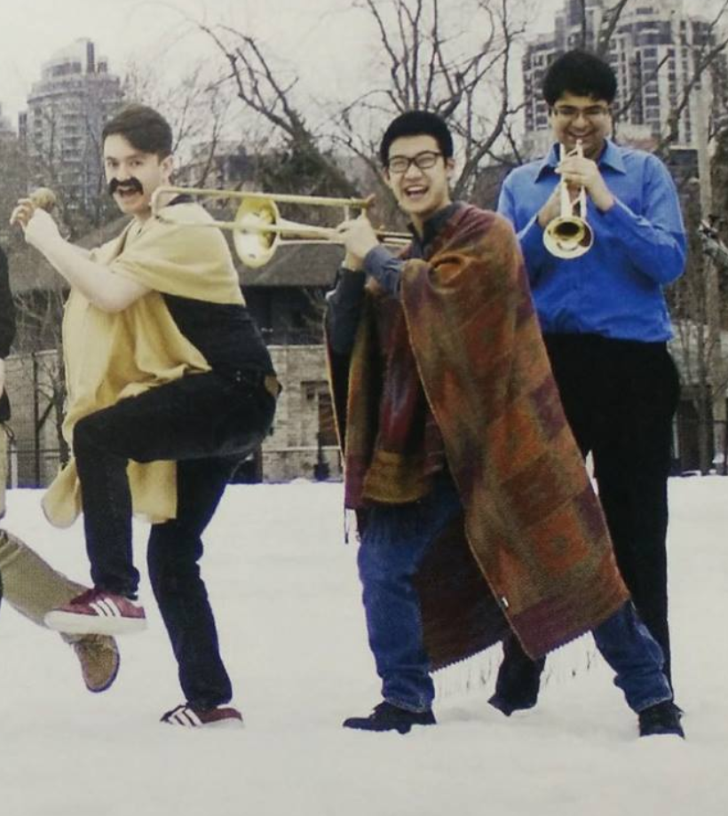 Three men in snow dancing with trumpets.