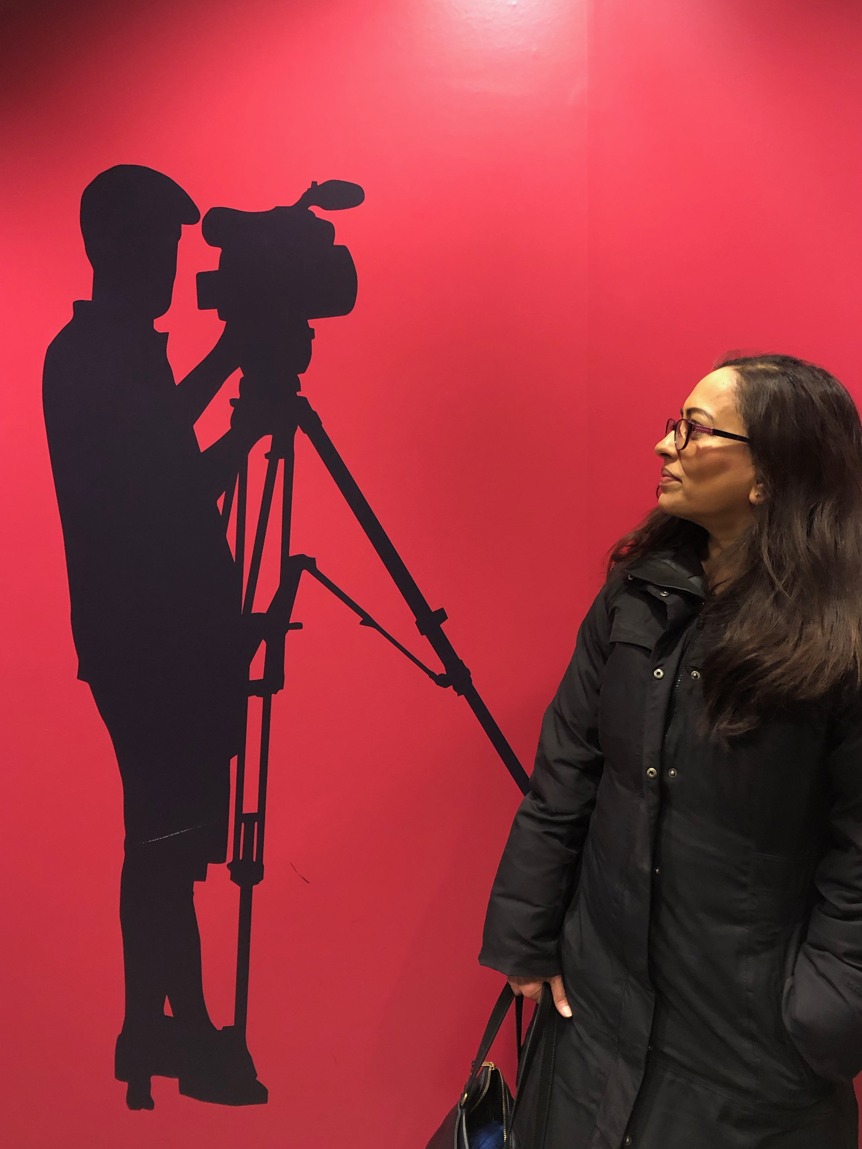 Woman looking at silhouette of man with camera on wall.