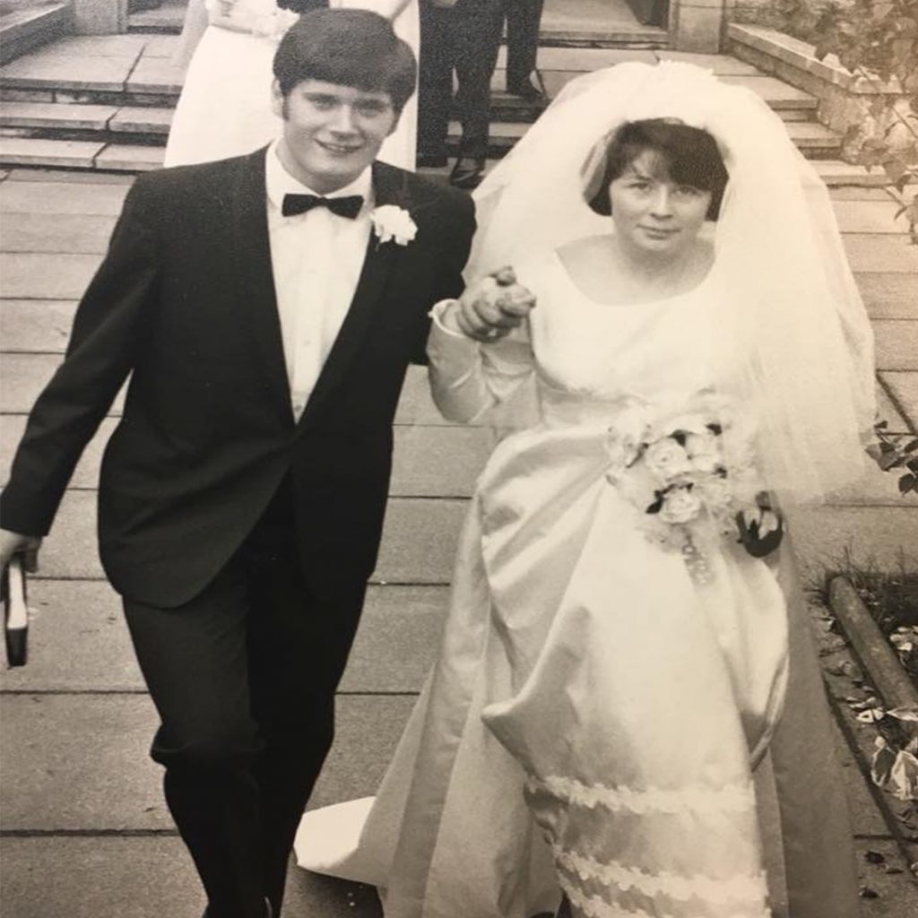 Black and white image of man in tuxedo and woman in wedding dress holding hands.