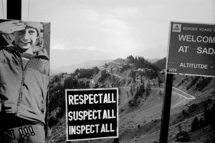 View of mountains with welcome sign, photo of young boy and sign reading "respect for all, suspect for all, inspect for all".