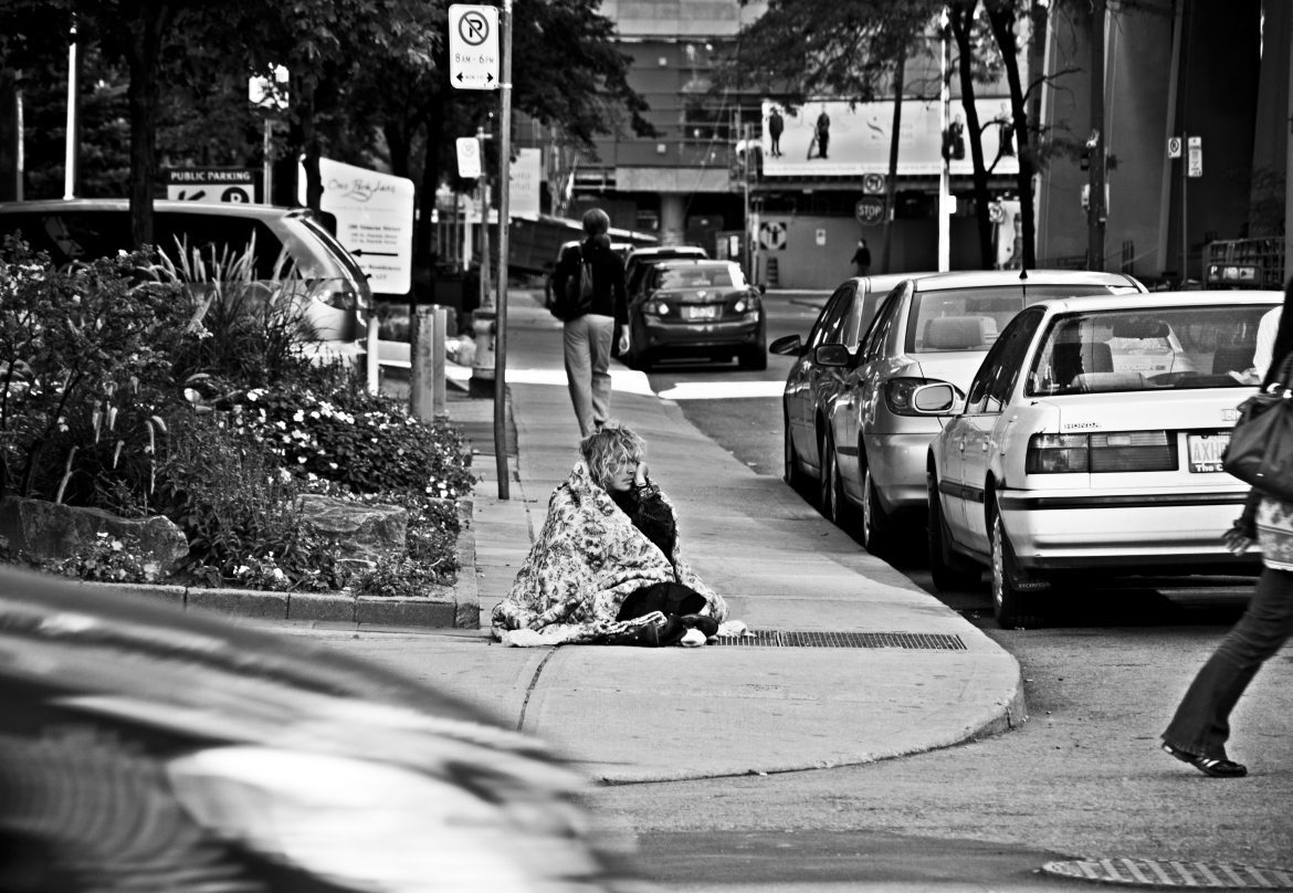 Woman sitting in blanket in middle of sidewalk.