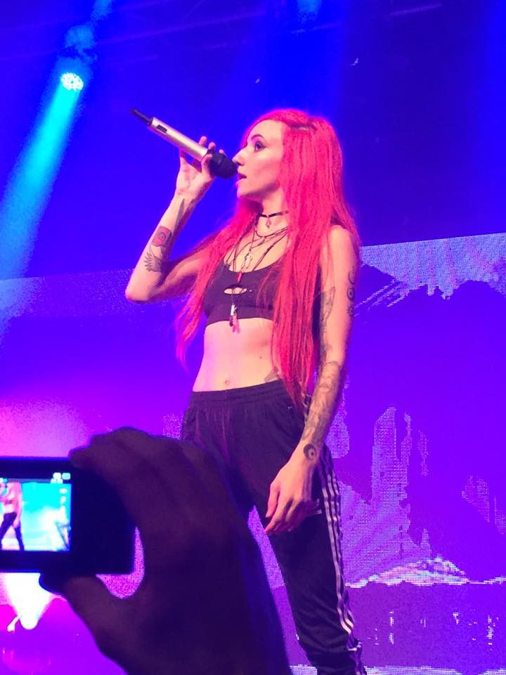 Woman with pink hair onstage holding microphone.