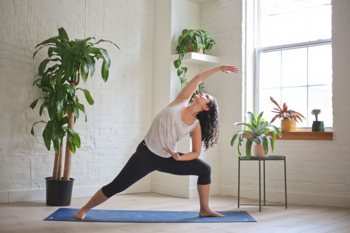 Woman on yoga mat surrounded by plants stretching.
