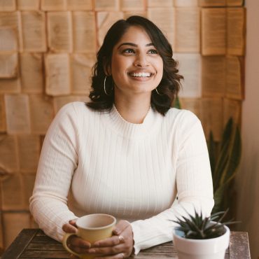 Woman holding mug in front of wall covered in books, smiling and looking away