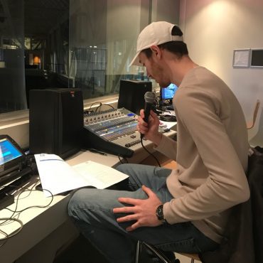 Braden Gibson holding a microphone practicing reads in a recording studio at the Mattamy Athletic Centre.