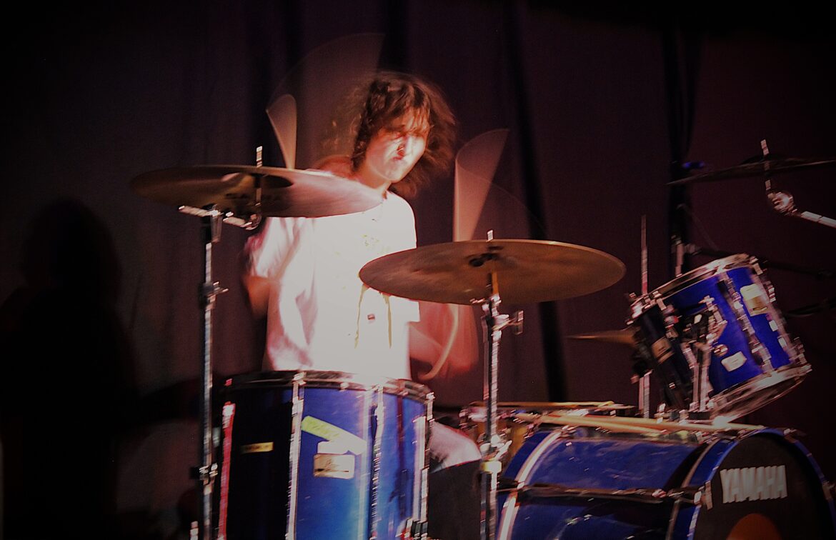 Woman with a curly brown bob playing the drums. 