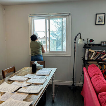 Women looking outside of window with her eating disorder research laid out on her dining table.