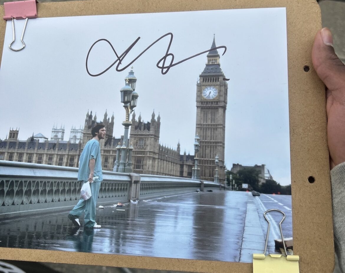 A signed photo of Cillian Murphy as Jim from 28 Days Later, walking alone across Westminster Bridge in London with Big Ben and the Houses of Parliament in the background on a deserted, rain-soaked street.